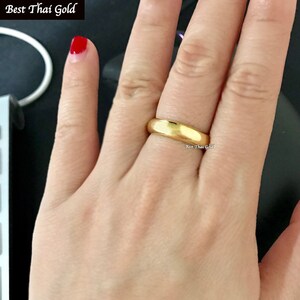 May include: A simple gold band ring worn on a finger. The ring is smooth and has a polished finish.