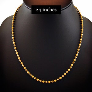 Pu&ograve; includere: Una collana a catena con perline dorate composta da una serie di piccole sfere uniformi collegate tra loro. La collana &egrave; esposta su un supporto nero e include un'etichetta rettangolare nera con il testo bianco 24 inches stampato sopra.