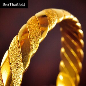May include: A gold bangle bracelet with a twisted design and a textured surface.
