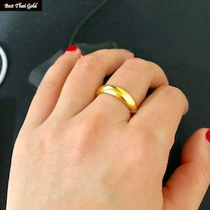 May include: A simple gold band ring worn on a finger.