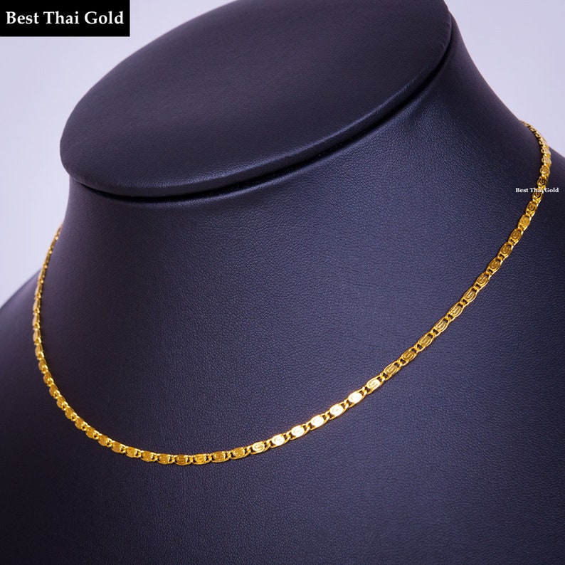 May include: A gold chain necklace featuring a series of interconnected, flat, oval-shaped links with a polished finish. The text 'Best Thai Gold' is visible in the upper left corner and on the right side of the chain.