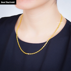 May include: A bright yellow gold chain necklace with a repeating textured link pattern. The necklace is worn around the neck and features the text Best Thai Gold in the upper left corner and a small watermark on the right side.