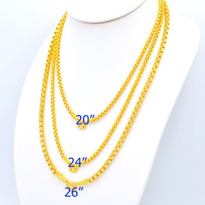 Puede incluir: Tres cadenas de oro de diferentes longitudes, 20 pulgadas, 24 pulgadas y 26 pulgadas, mostradas en un maniquí blanco.
