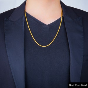 May include: A gold chain necklace on a person wearing a black shirt and jacket. The chain is a rope style with a fine, delicate design. The text "Best Thai Gold" is visible at the bottom of the image.