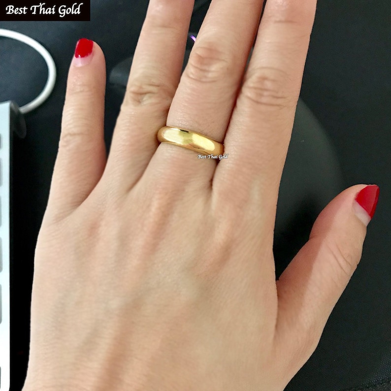 May include: A simple gold band ring worn on a finger. The ring is smooth and has a polished finish.