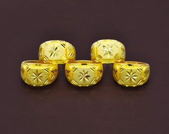 May include: Five gold rings arranged in two rows, each featuring a wide band with a textured surface and a central engraved star pattern. The rings have a polished finish and a consistent design with geometric detailing along the sides of the bands.