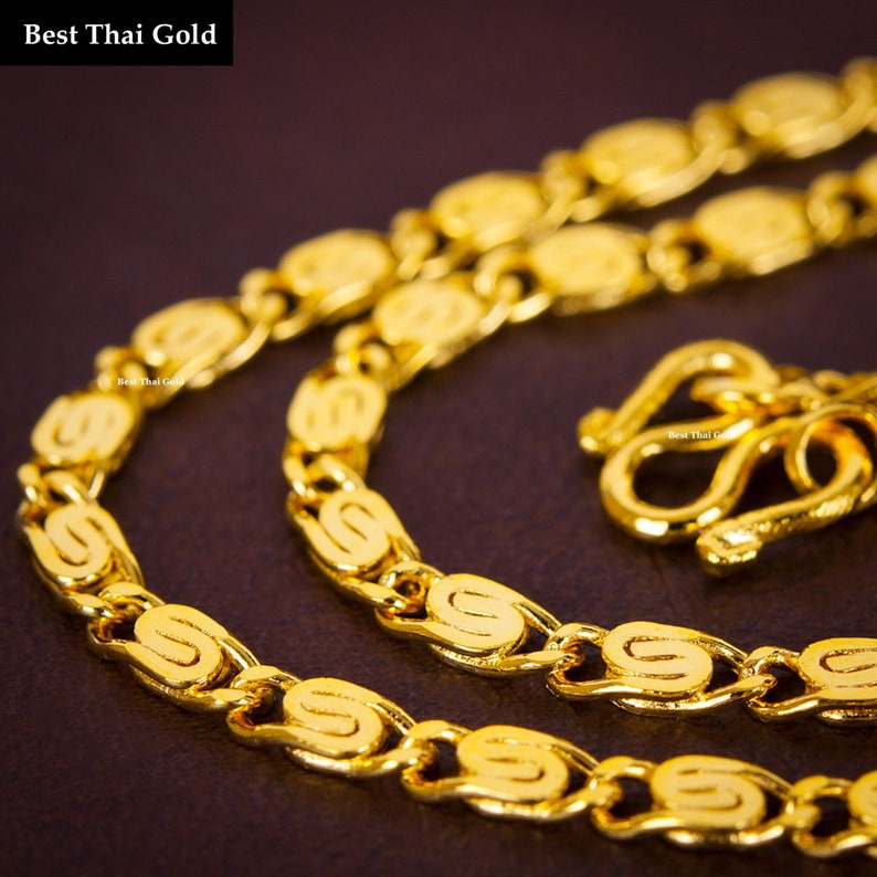 May include: A bright yellow gold chain necklace featuring repeating S-shaped links and a secure hook clasp. The text Best Thai Gold is visible in the upper left corner and repeated in small print on the chain links and the clasp mechanism.