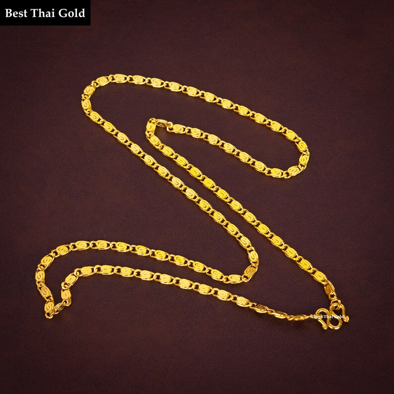 May include: A bright yellow gold chain necklace featuring a repeating pattern of interlocking oval links with a textured, swirling design. The necklace includes a secure S-hook clasp at one end and displays the text Best Thai Gold.