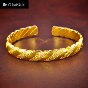 May include: A gold-colored bangle bracelet with a twisted design and a textured surface.