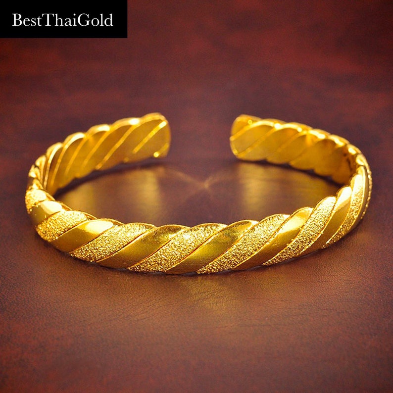 May include: A gold-colored bangle bracelet with a twisted design and a textured surface.