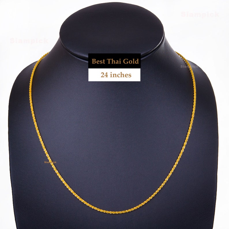 May include: A gold chain necklace on a black display stand. The chain is 24 inches long and has a delicate, braided design. The text "Best Thai Gold" is printed on a white label.