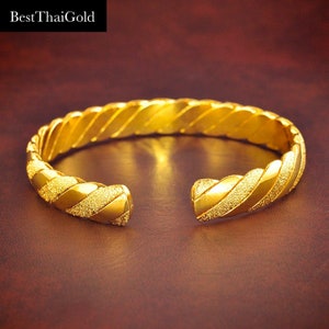 May include: A gold bangle bracelet with a twisted design and a textured finish.