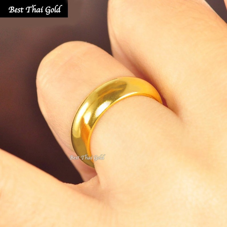 May include: A simple gold band ring worn on a finger. The ring is smooth and shiny.