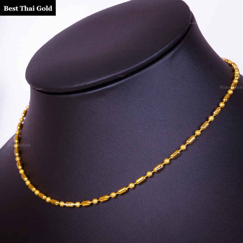 May include: A gold chain necklace featuring an alternating pattern of small, textured spherical beads and smooth, elongated cylindrical links. The text "Best Thai Gold" is visible in the upper left corner of the image.