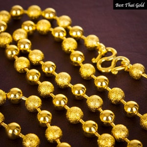 Pu&ograve; includere: Una collana a catena in oro caratterizzata da un'alternanza di perline sferiche lisce e lucide e perline con finitura opaca testurizzata. La collana include una chiusura a gancio in oro e il testo Best Thai Gold &egrave; visibile nell'angolo e sulla chiusura.