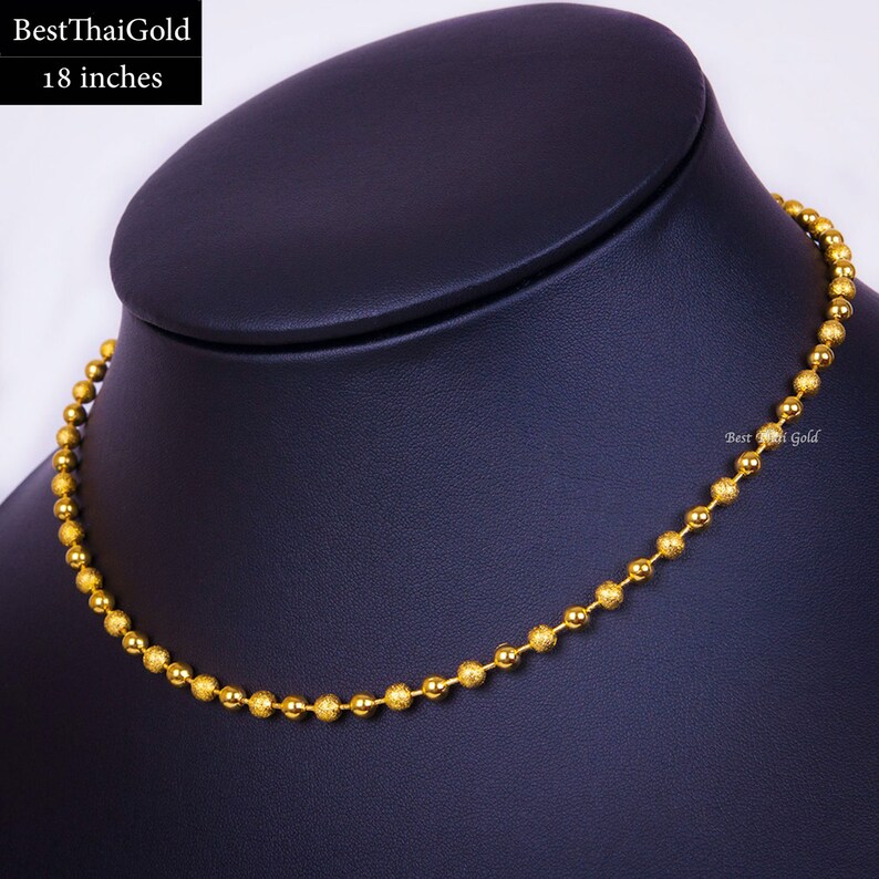 Pu&ograve; includere: Una collana a catena con sfere dorate lunga 18 pollici. La collana &egrave; composta da un'alternanza di sfere d'oro lisce e lucide e sfere d'oro testurizzate con finitura opaca. Il testo BestThaiGold &egrave; visibile nell'angolo in alto a sinistra.