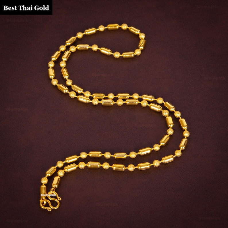 May include: A gold chain necklace featuring alternating smooth cylindrical beads and textured spherical beads. The necklace includes a secure S-hook clasp at the end. The text Best Thai Gold is visible in the upper left corner of the image.