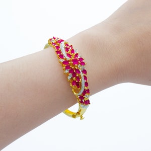 May include: A gold bangle bracelet with a floral design featuring pink and white stones.