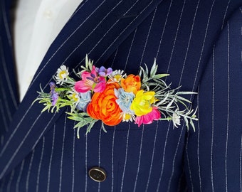 May include: A navy blue suit jacket with thin white pinstripes. The jacket has a double breasted closure with two gold buttons. A small bouquet of colorful flowers is pinned to the lapel.