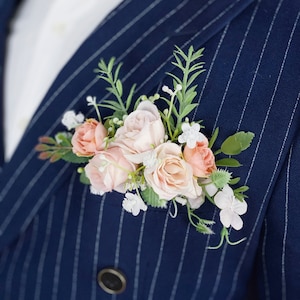 Puede incluir: Una chaqueta de traje azul marino con un patrón de rayas blancas. Un pequeño ramo de flores rosas y blancas está prendido en la solapa.