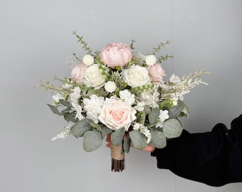 Pode incluir: Um buquê de noiva com rosas brancas e rosa claro, folhagem e bagas brancas.