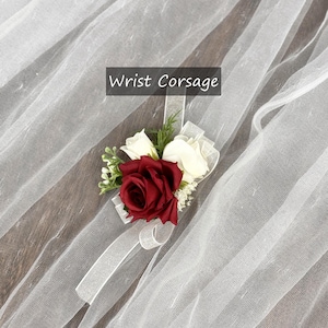 May include: A red and white wrist corsage with a white ribbon. "Wrist Corsage" is written in black text on a white background.