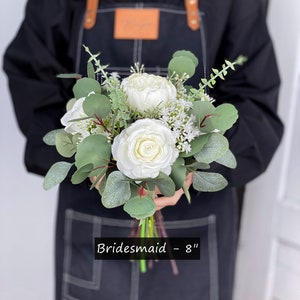 May include: A white bridesmaid bouquet with eucalyptus greenery and white flowers. The bouquet is 8 inches in diameter. "Bridemaid - 8" is written on the bottom of the image.
