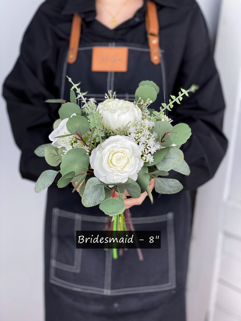 May include: A white bridesmaid bouquet with eucalyptus greenery and white flowers. The bouquet is 8 inches in diameter. "Bridemaid - 8" is written on the bottom of the image.