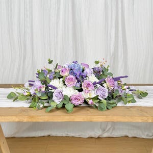 Peut inclure: Une composition florale de couleur pourpre et blanche avec de la verdure, idéale pour une pièce maîtresse de mariage ou d'événement spécial.