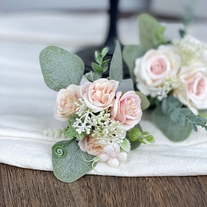 May include: A small bouquet of blush pink roses and white flowers with green eucalyptus leaves.