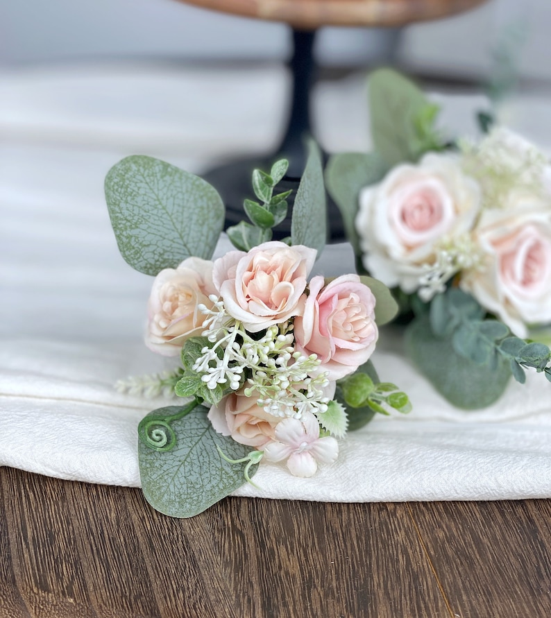May include: A small bouquet of blush pink roses and white flowers with green eucalyptus leaves.
