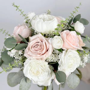 May include: A bridal bouquet featuring white and blush pink roses, white ranunculus, and greenery.