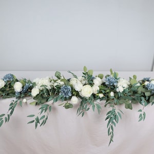 Könnte beinhalten: Eine künstliche Blumenkette in Weiß und Blau mit Grün. Die Girlande besteht aus weißen Rosen, blauen Hortensien und Eukalyptusblättern.