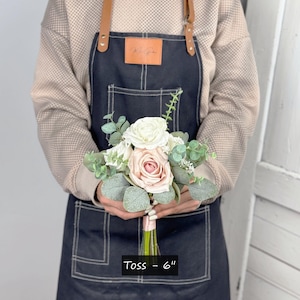 May include: A small bouquet of blush pink and white roses with greenery, tied with a blush pink ribbon. The bouquet is labelled "Toss - 6" inches.