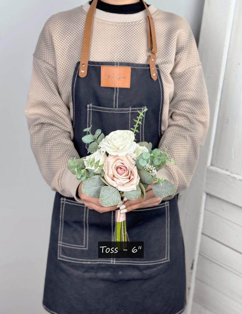 May include: A small bouquet of blush pink and white roses with greenery, tied with a blush pink ribbon. The bouquet is labelled "Toss - 6" inches.