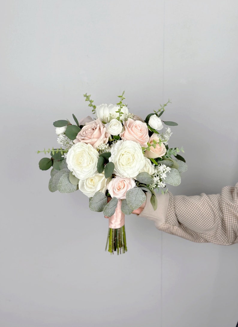 May include: A bridal bouquet featuring white and blush roses, eucalyptus, and white baby's breath.