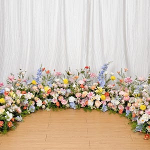 May include: A floral archway made of pastel pink, yellow, blue, and white flowers. The archway is made of real flowers and is perfect for a wedding or other special event.
