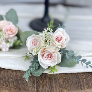 May include: A small bouquet of blush pink roses with greenery, ideal for a wedding or special occasion.