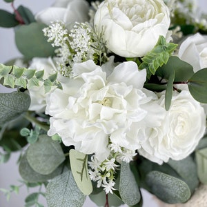 May include: A bouquet of white peonies, roses, and small white flowers with eucalyptus leaves.