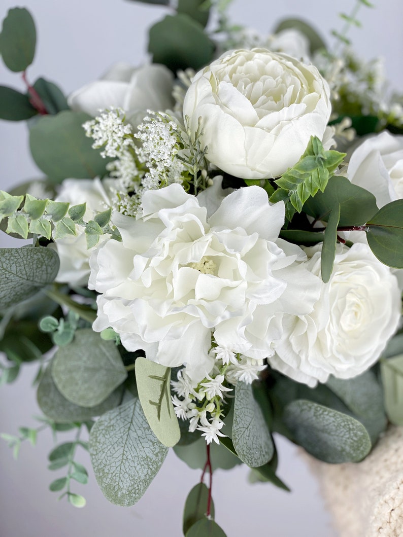 May include: A bouquet of white peonies, roses, and small white flowers with eucalyptus leaves.