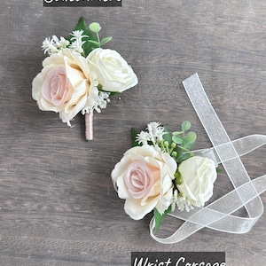 May include: Two white and blush pink rose buttonholes with greenery and white ribbon. The buttonhole on the left is labelled "Boutonniere" and the buttonhole on the right is labelled "Wrist Corsage".
