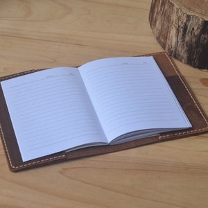 May include: A brown leather bound journal with lined pages. The journal is open to reveal the blank pages.