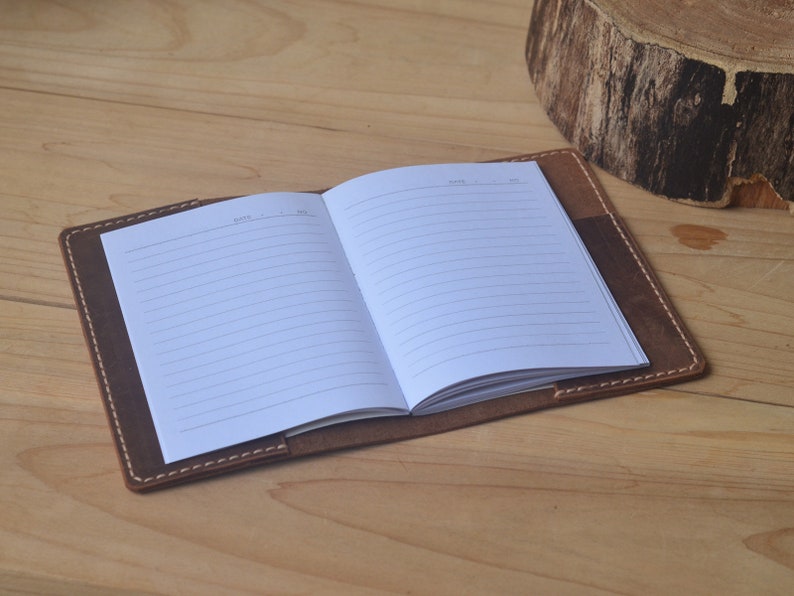 May include: A brown leather bound journal with lined pages. The journal is open to reveal the blank pages.
