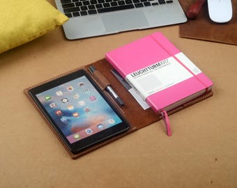 Könnte beinhalten: Eine braune Leder-Notizbuchhülle mit einem rosa Notizbuch im Inneren. Die Notizbuchhülle hat einen Schlitz für einen Stift und ein Tablet. Die Notizbuchhülle trägt den Text "LEUCHTTURM1917" auf der Vorderseite.