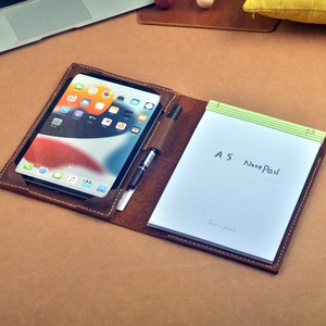 May include: A brown leather folio with a tablet and a notepad. The notepad has a green lined paper and says "A5 NotePad" on the front.