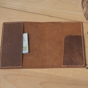 May include: A brown leather wallet with a white stitch detail and a pocket for cash or cards. The wallet is open and a twenty euro bill is visible in the pocket.