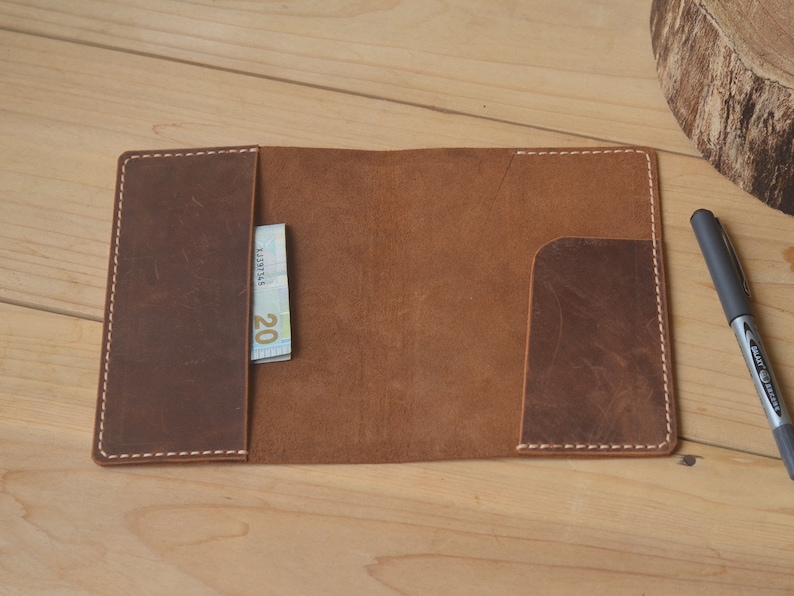 May include: A brown leather wallet with a white stitch detail and a pocket for cash or cards. The wallet is open and a twenty euro bill is visible in the pocket.