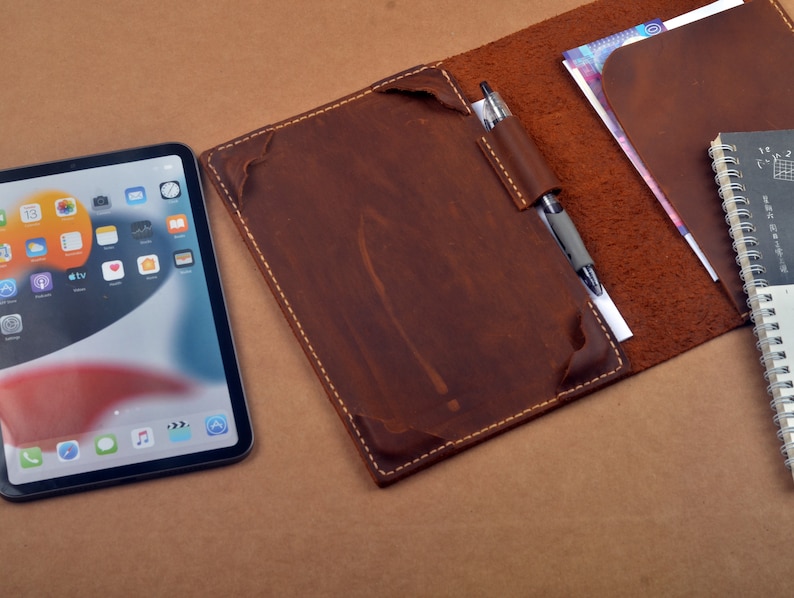May include: A brown leather portfolio with a pen, a notebook, and a tablet computer. The portfolio has a flap that closes with a snap.