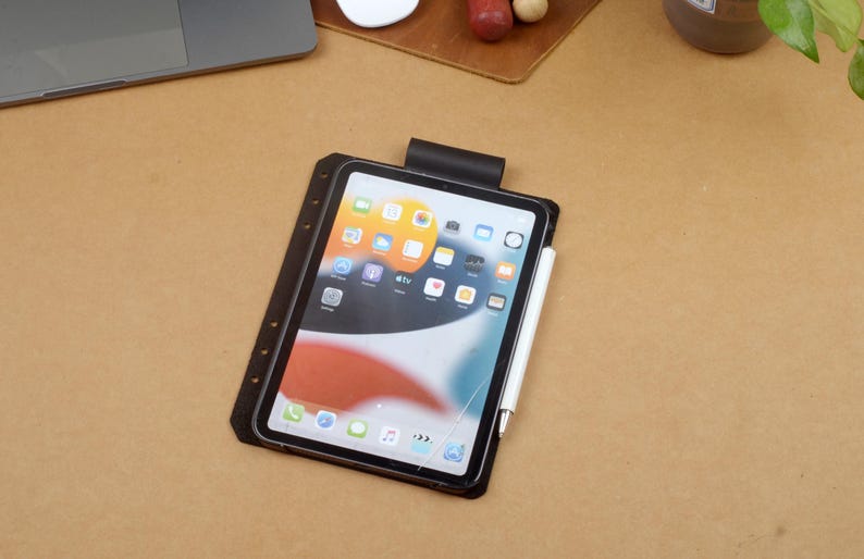 Może przedstawiać: Czarny tablet z dołączonym białym rysikiem, spoczywający na brązowej powierzchni. Tablet wyświetla kolorowy ekran aplikacji. Tablet jest w czarnym etui z klipsem na g&oacute;rze.