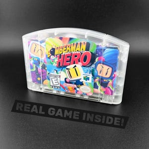 May include: A clear plastic Nintendo 64 game cartridge for Bomberman Hero. The label features the title in bold red and black text, a white character with a bomb, and an ESRB Everyone rating. The cartridge has a transparent shell design.